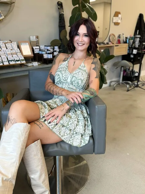 Em smiling in the salon chair, short dark-red waves, hoop earrings.